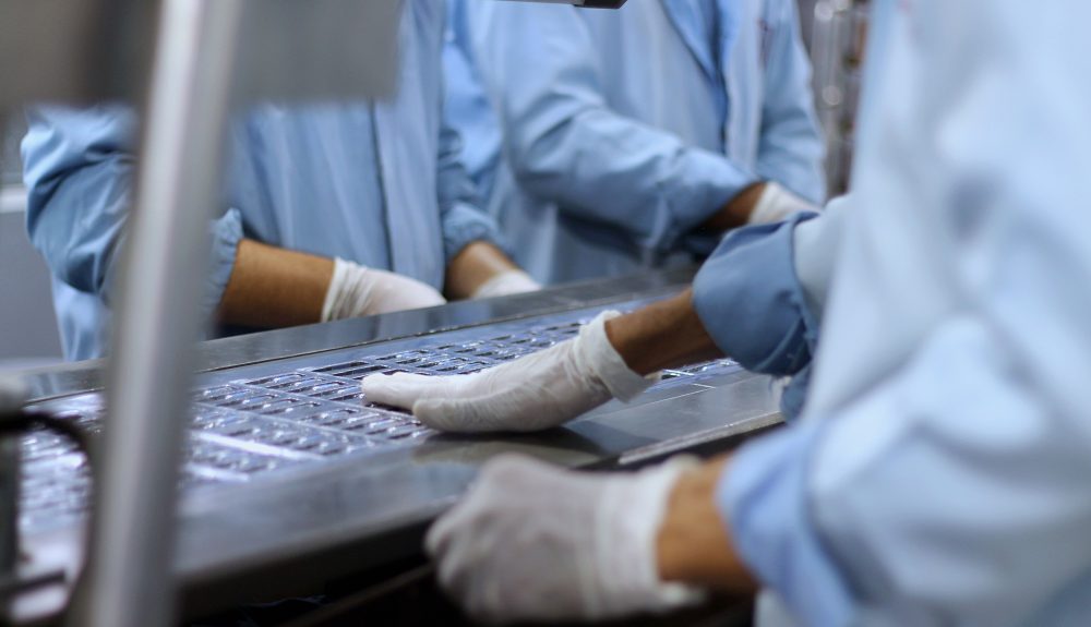 Workers in a pharmaceutical facility packaging tablets, tied to Coretime for pharma consultant time and project management.