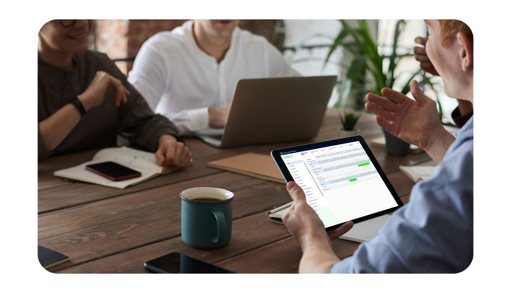Team of colleagues gathered around a table, with one using an iPad to view the coretime leave chart for shared planning.